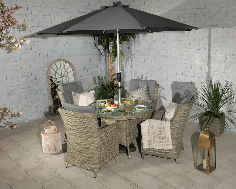 Rattan outdoor dining set with glass table, six cushioned chairs and grey parasol on patio