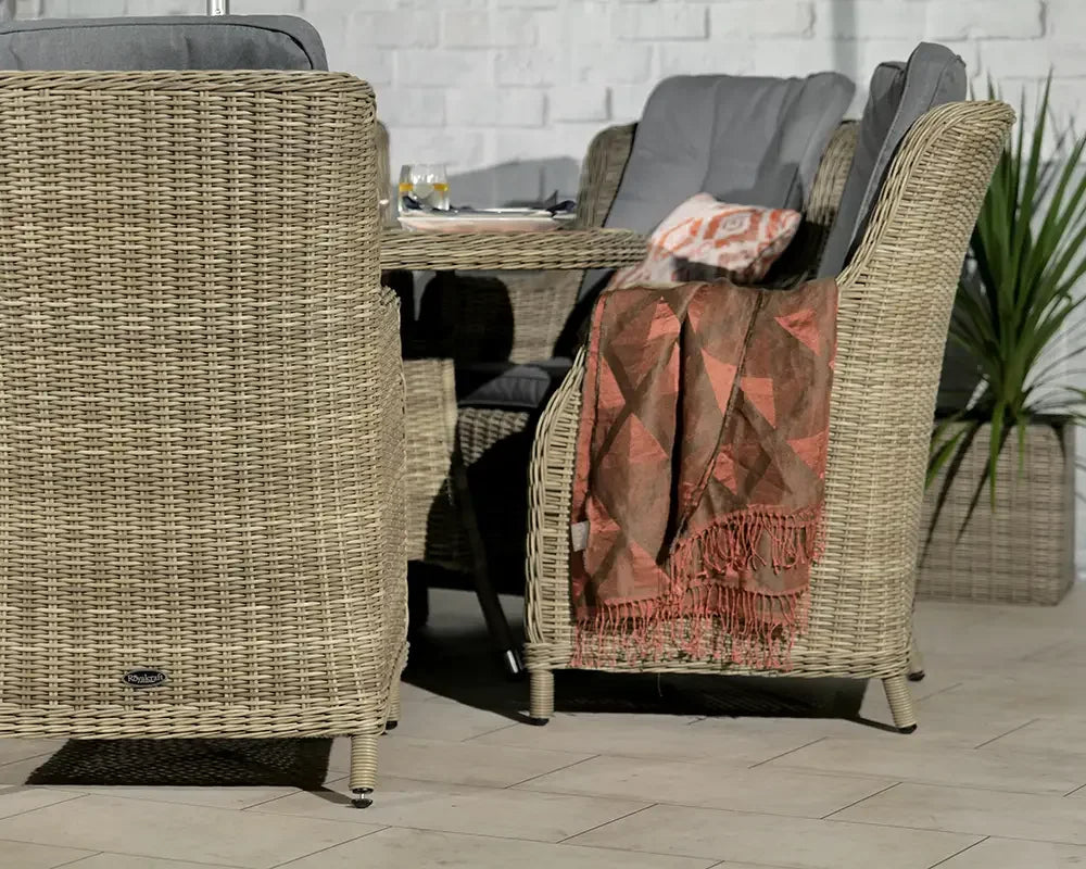 Rattan dining set with grey cushions and throw, set against a white brick wall with plant decor