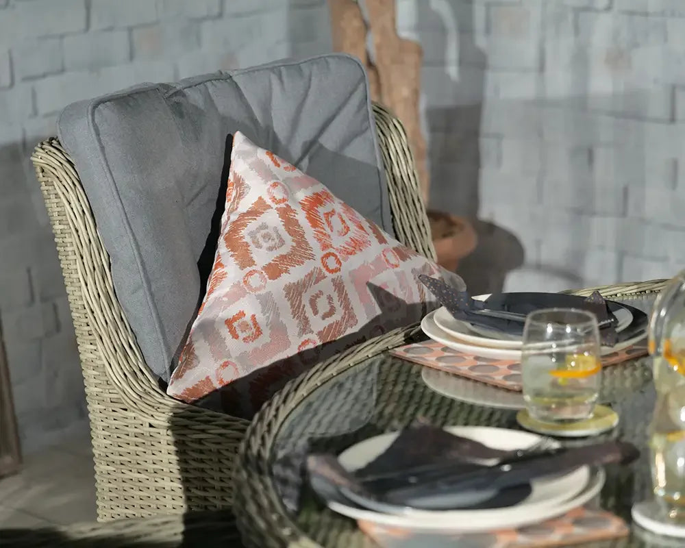 Wicker dining chair with grey cushion and patterned pillow beside glass dining table with place settings