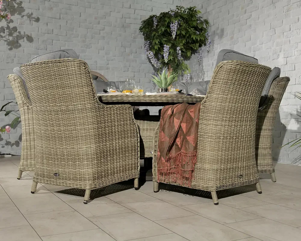Rattan dining set with four armchairs, round table, and cushions in a garden patio setting