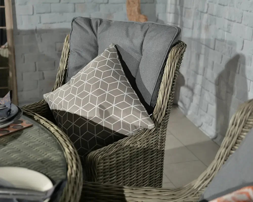 Wicker dining chair with grey cushion and geometric patterned pillow next to round glass table