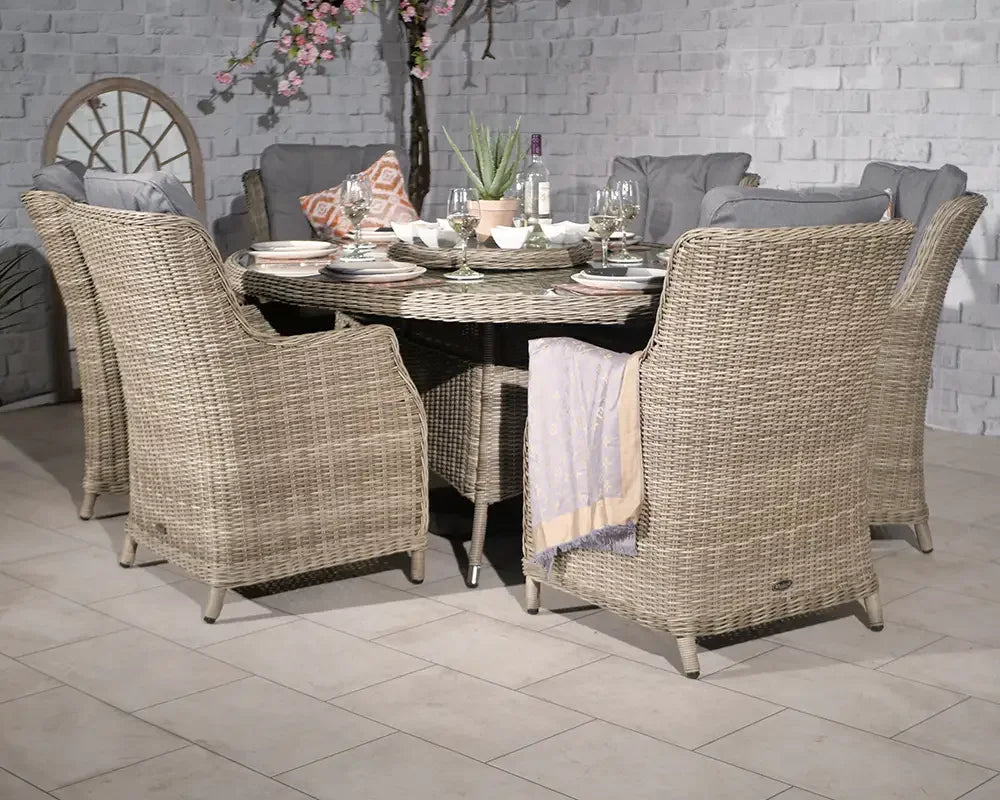 Round rattan dining set with six cushioned chairs and a table set for dinner indoors