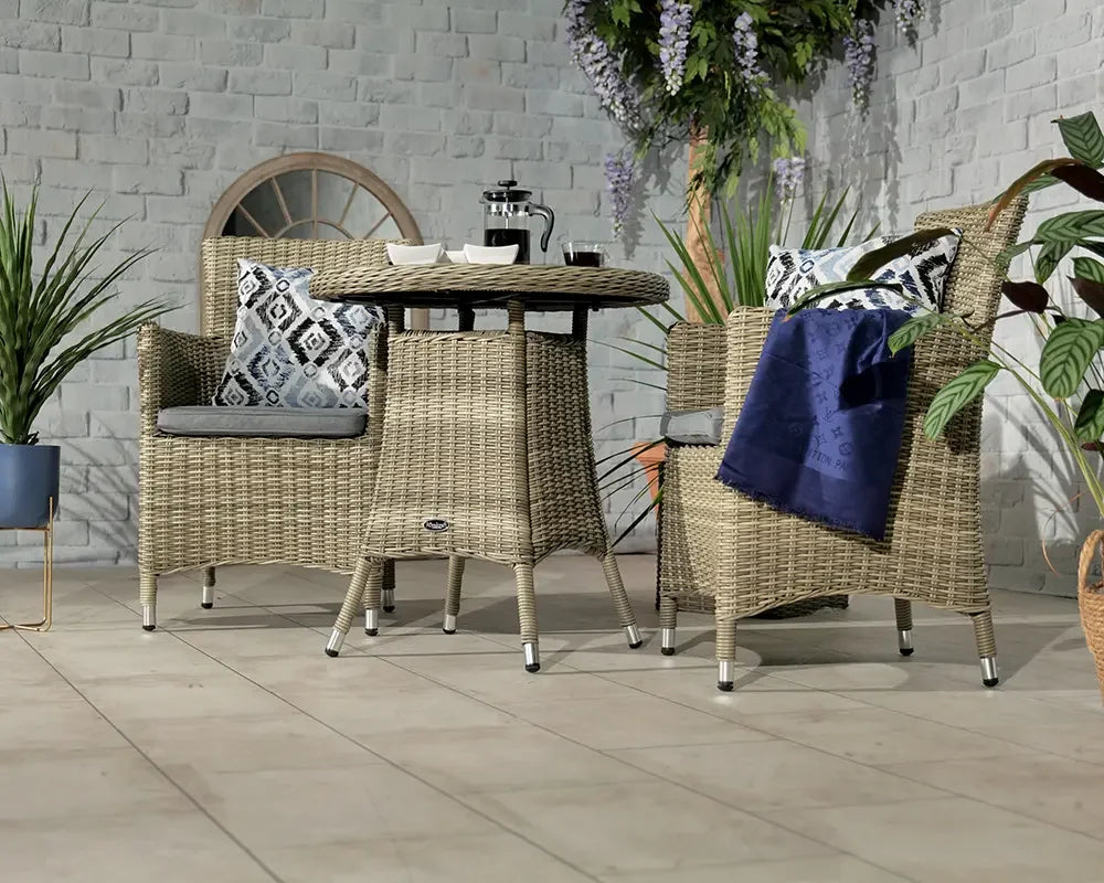 Rattan garden dining set with two armchairs, cushions, and a rectangular table on patio