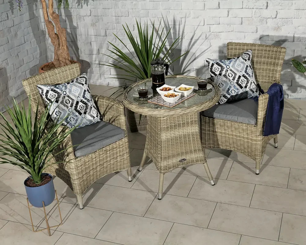 Rattan bistro set with glass-top table, two grey cushioned chairs and patterned cushions