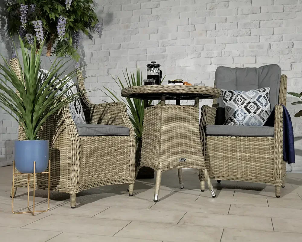 Rattan garden bistro set with two armchairs, grey cushions and round table indoors