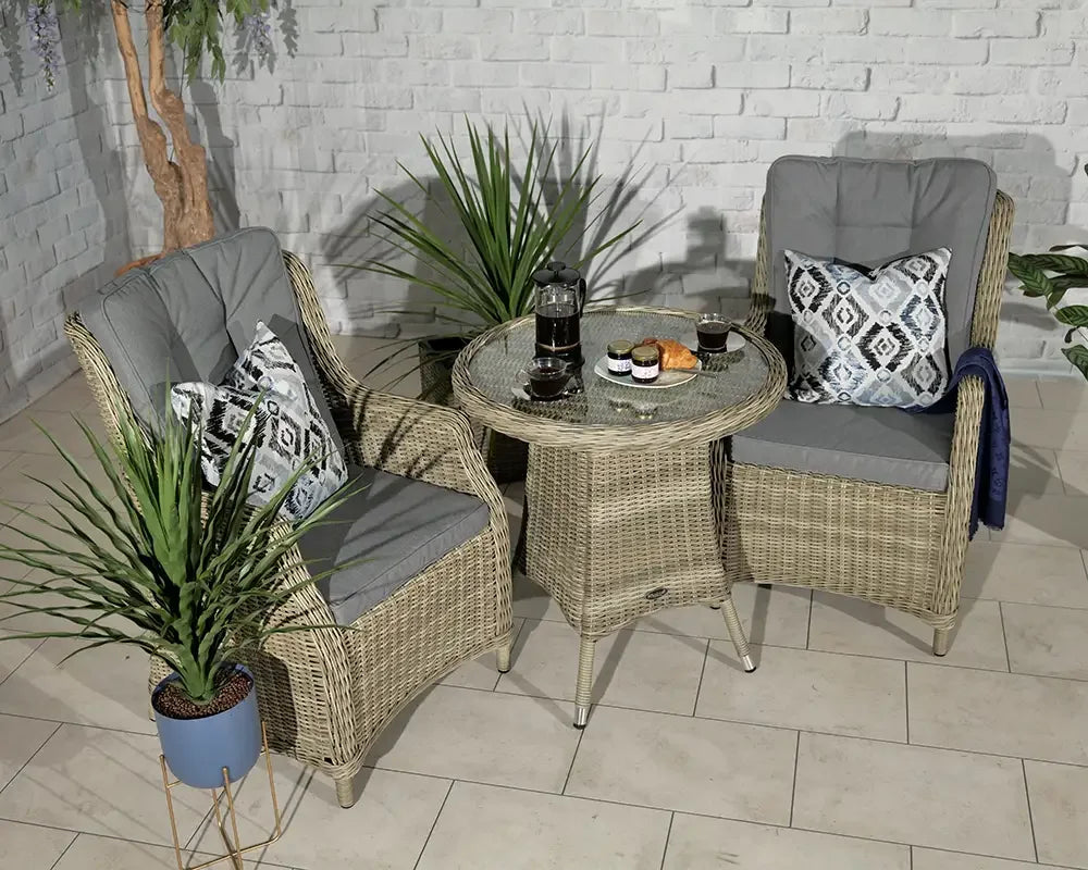 Rattan bistro set with two cushioned chairs and round glass table in indoor setting