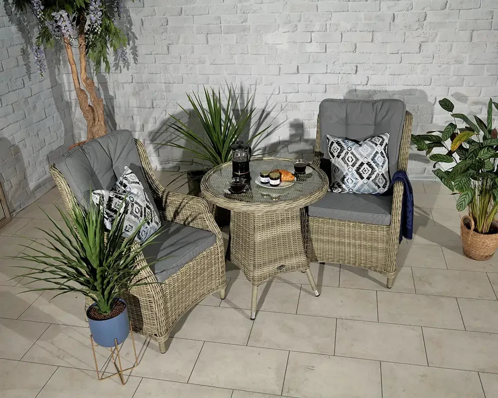 Rattan bistro set with two grey cushioned chairs and glass table in a modern indoor setting