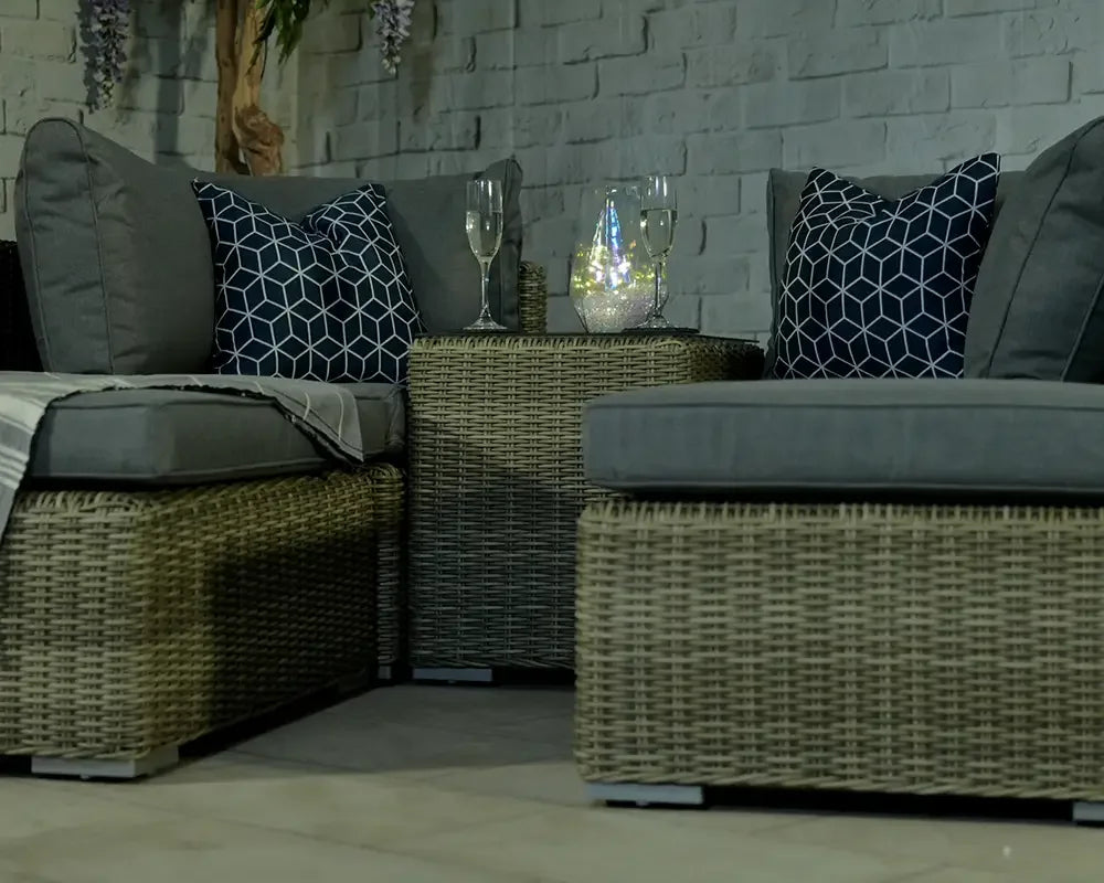 Rattan garden furniture set with grey cushions, patterned pillows and glass tabletop