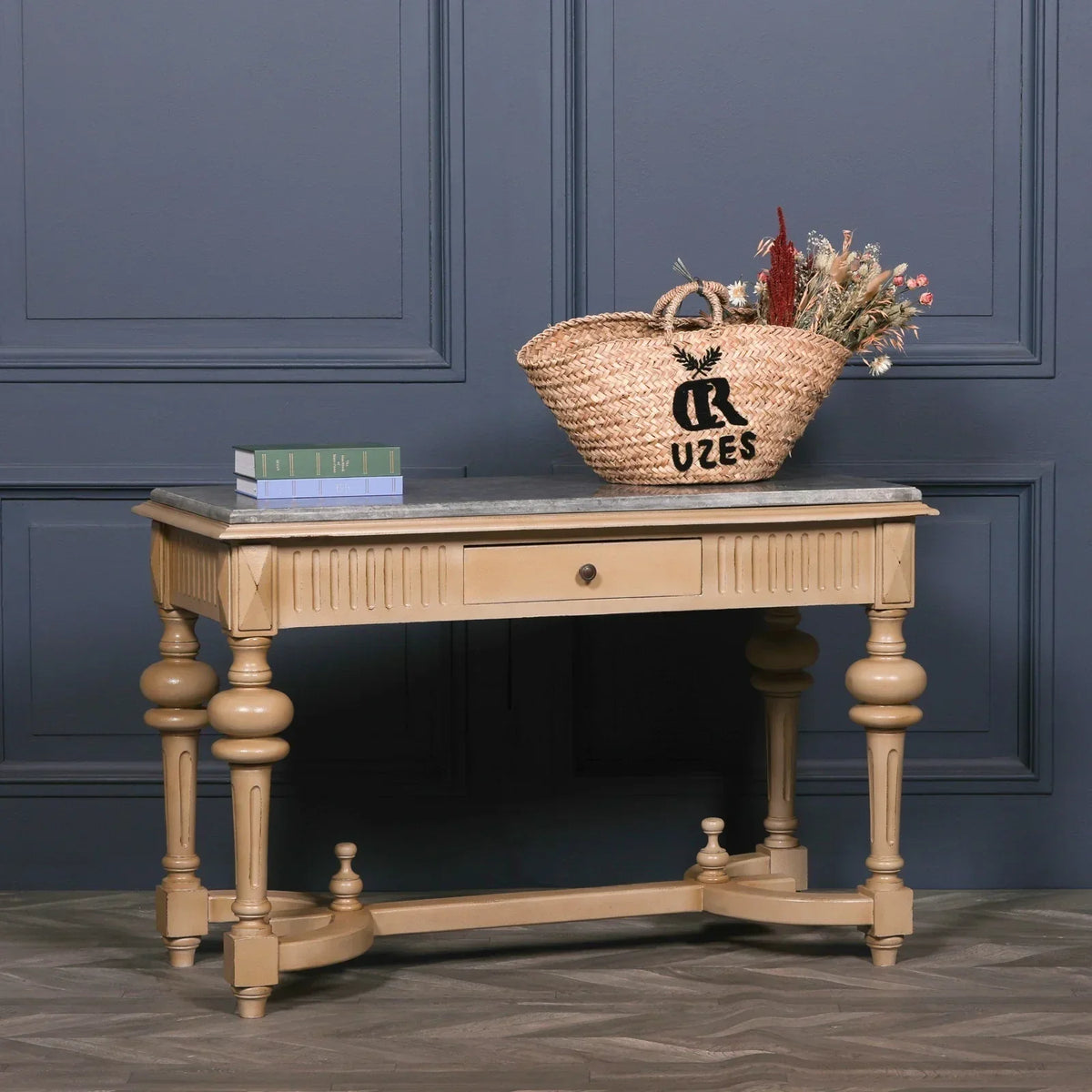 Wood console table with carved legs, stone top, front drawer, basket and books displayed