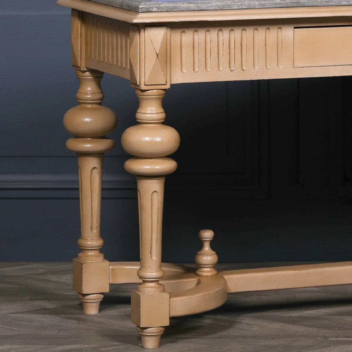 Wooden console table leg with ornate turned design and light brown finish on herringbone floor