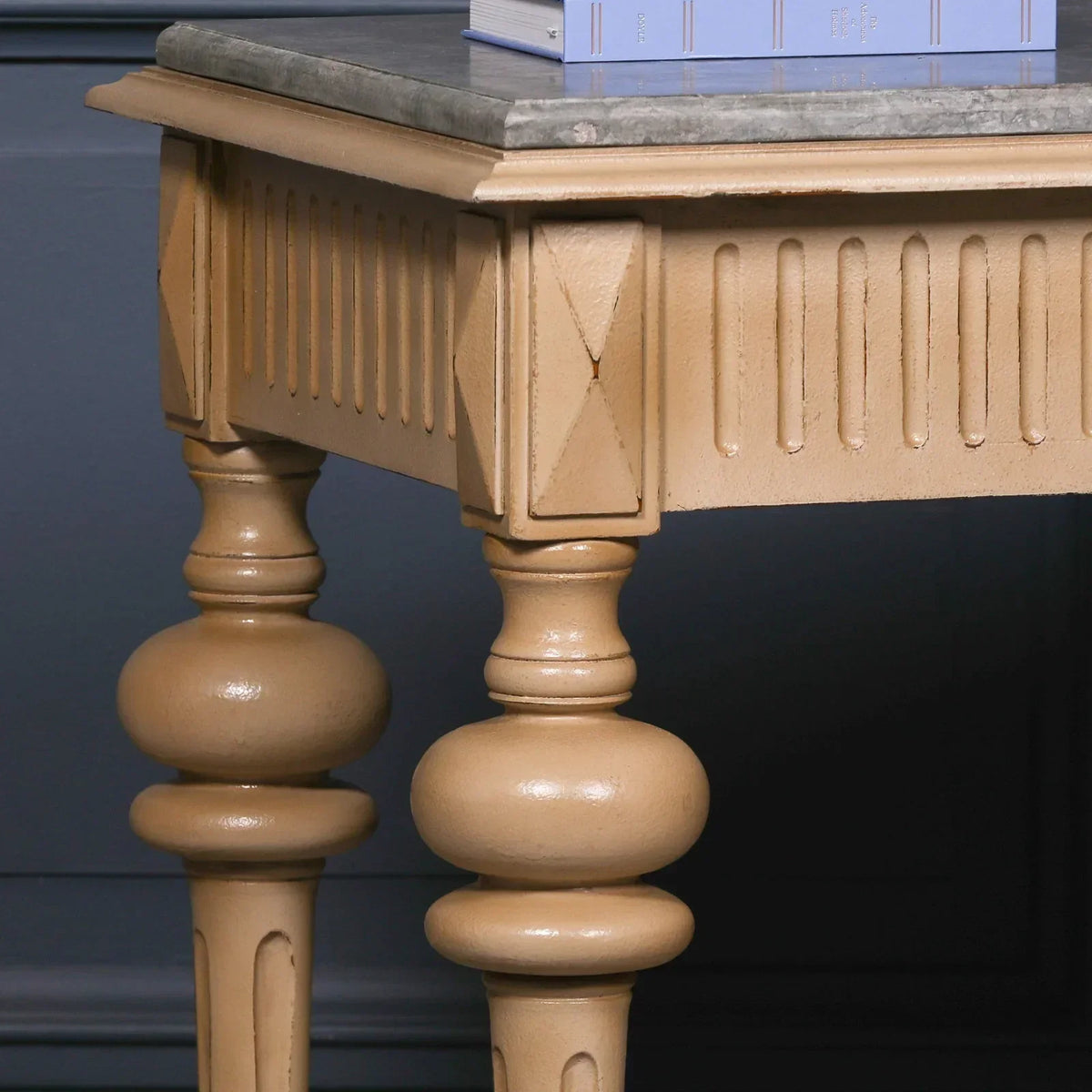 Beige wooden side table with carved legs and a stone top against dark wall