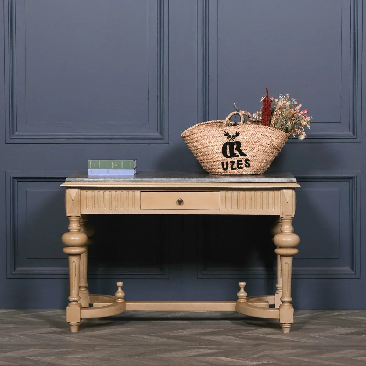 Wood console table with single drawer, marble top, basket and books, set against blue wall