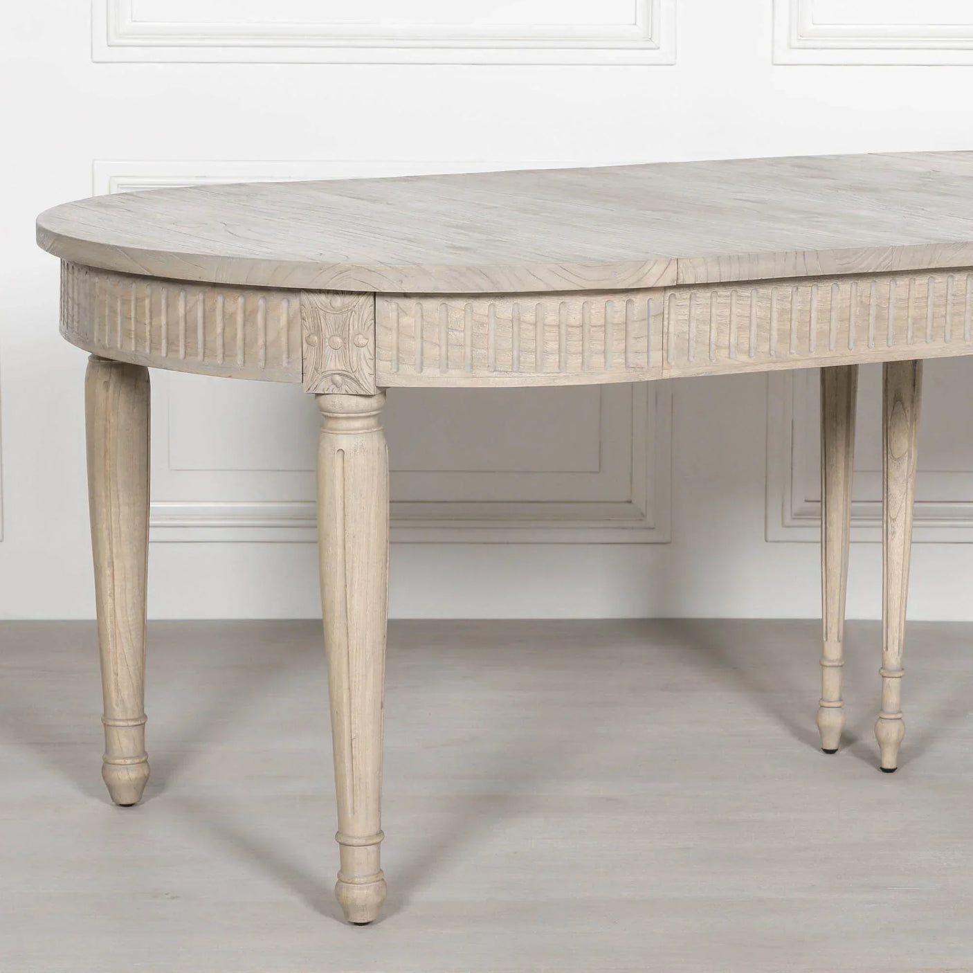 Light wood dining table with carved apron and tapered legs against white panel wall