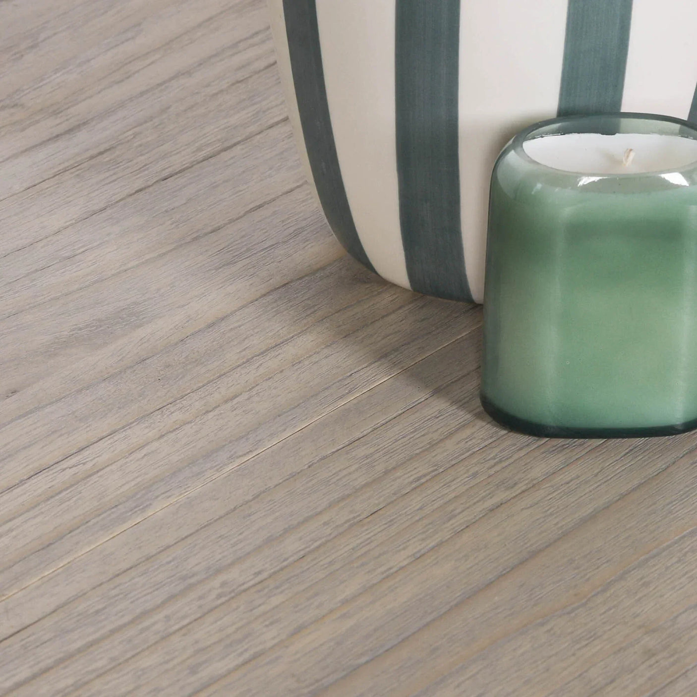 Close view of wood dining table surface with green candle and striped ceramic vase