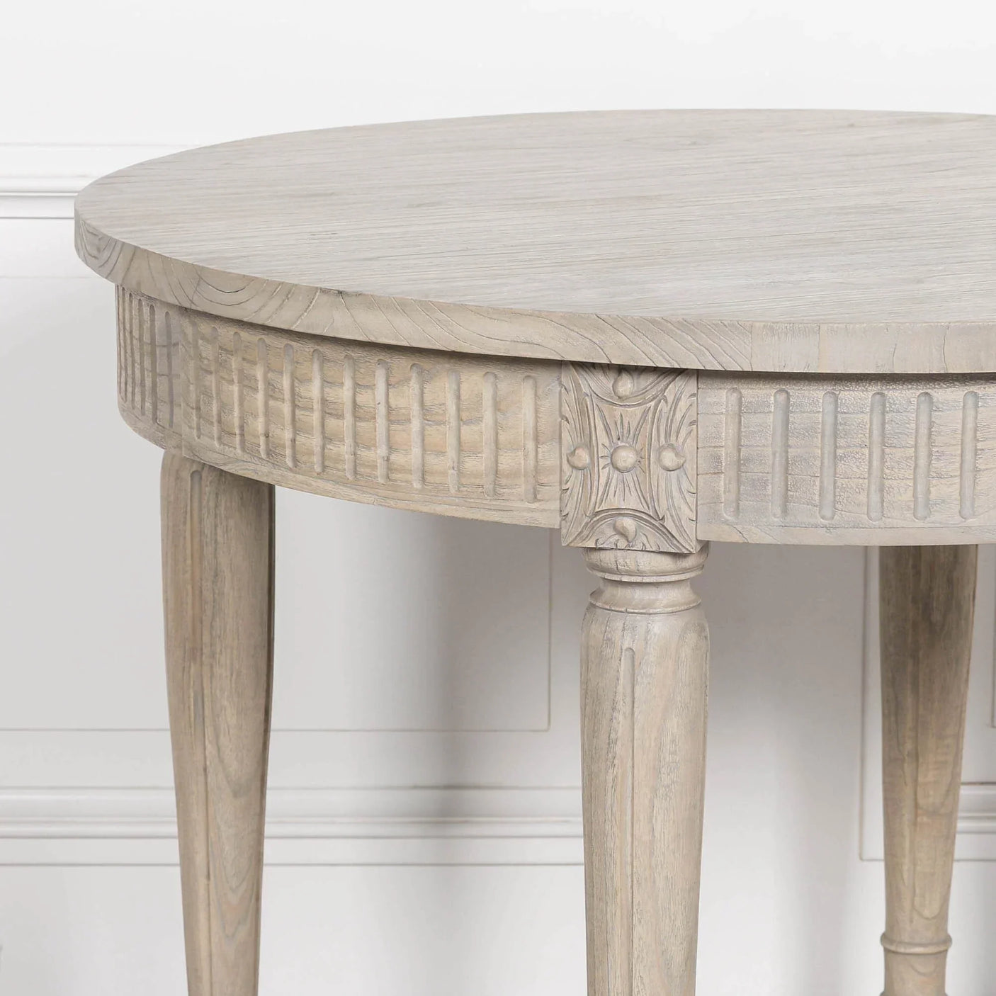Round wooden accent table with carved legs and fluted detailing against white wall