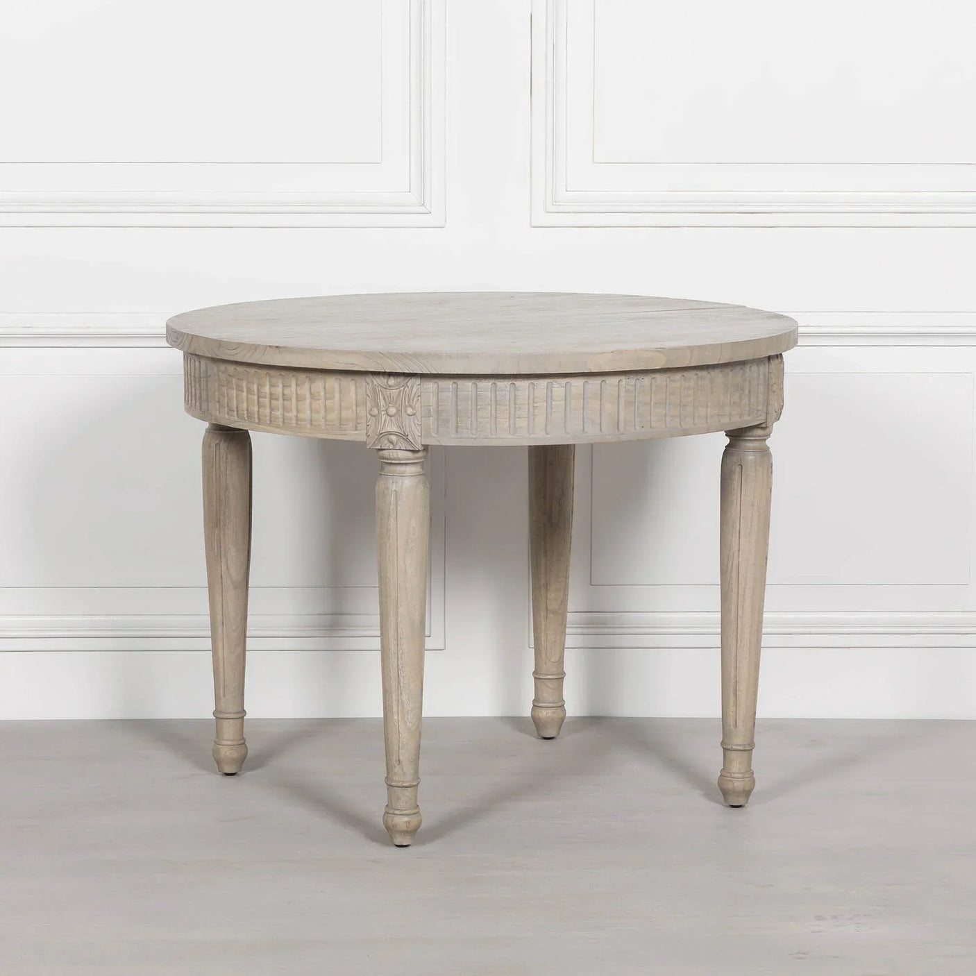 Round oak dining table with fluted legs and carved detailing in light wood finish