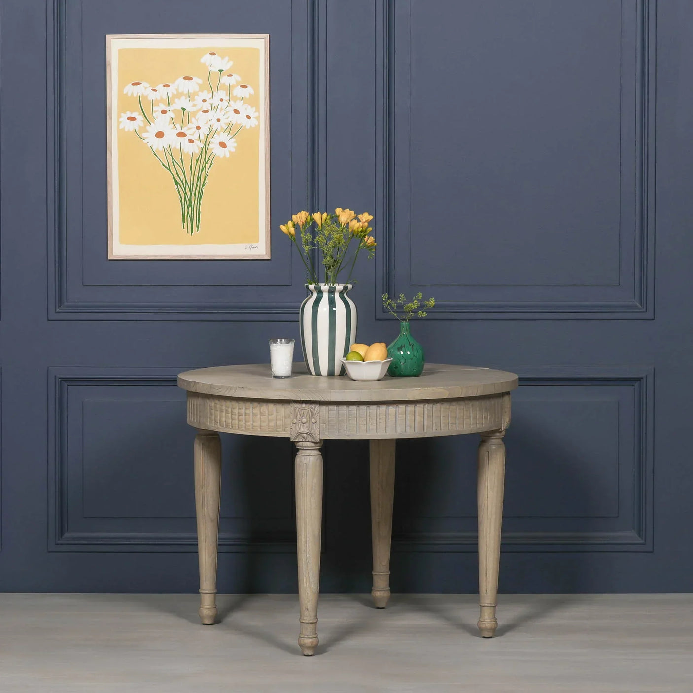 Round wooden dining table with carved legs styled with vases and fruit bowl against blue wall
