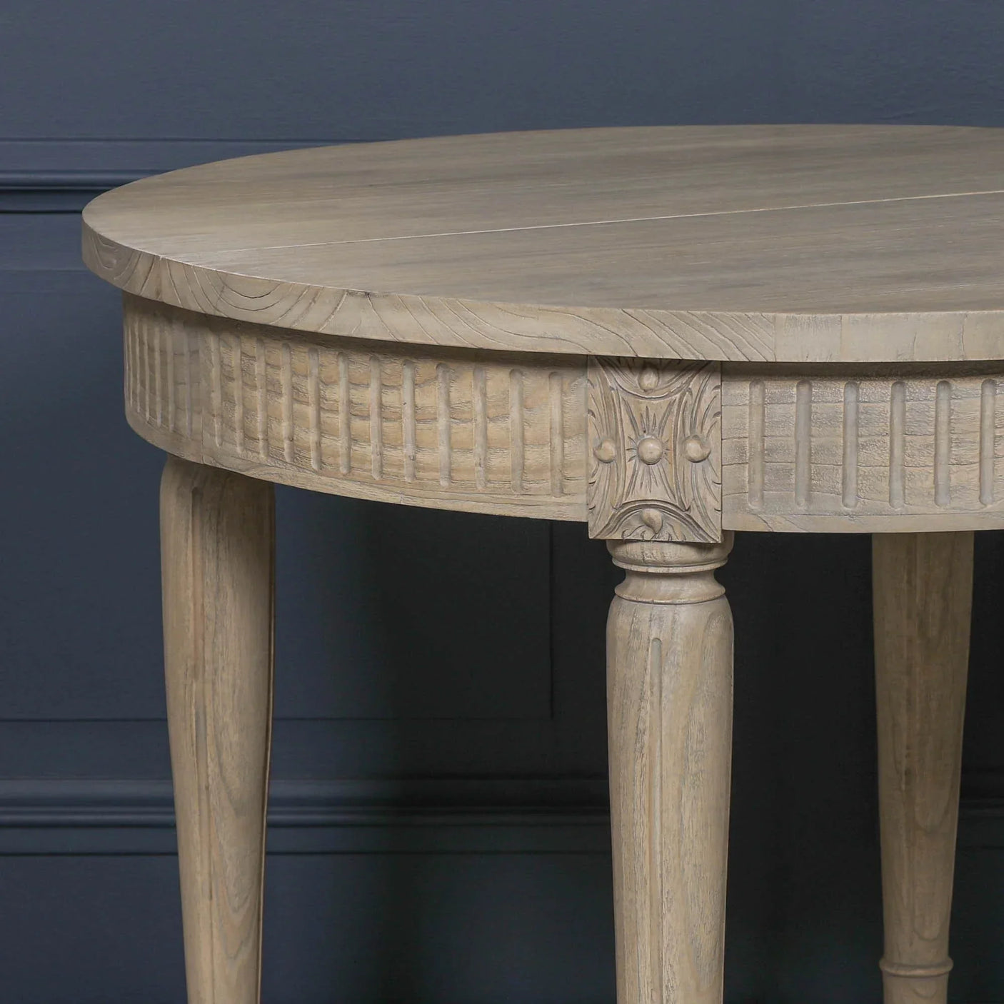 Round wooden dining table with carved detailing and tapered legs against dark wall