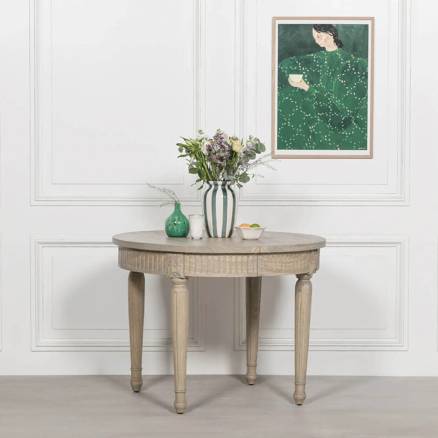 Round wooden dining table with carved legs, styled with vases and flowers in modern room