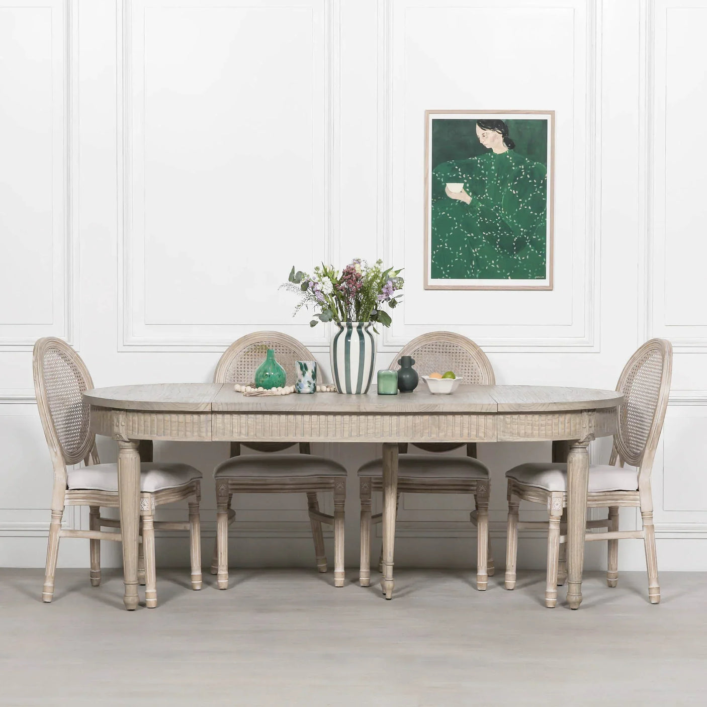 Oval wood dining table with six cane back chairs and striped vase centerpiece