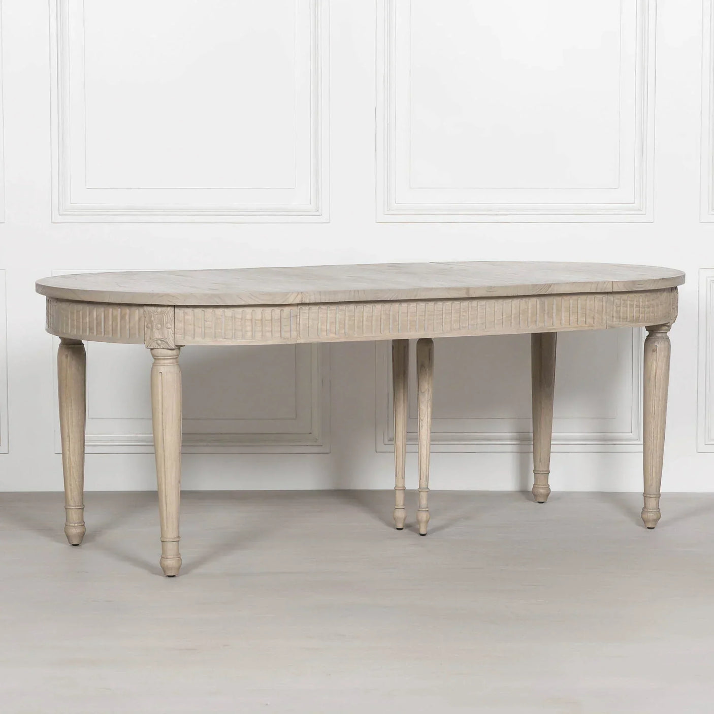 Oval wooden dining table with carved edge and turned legs against white panel wall