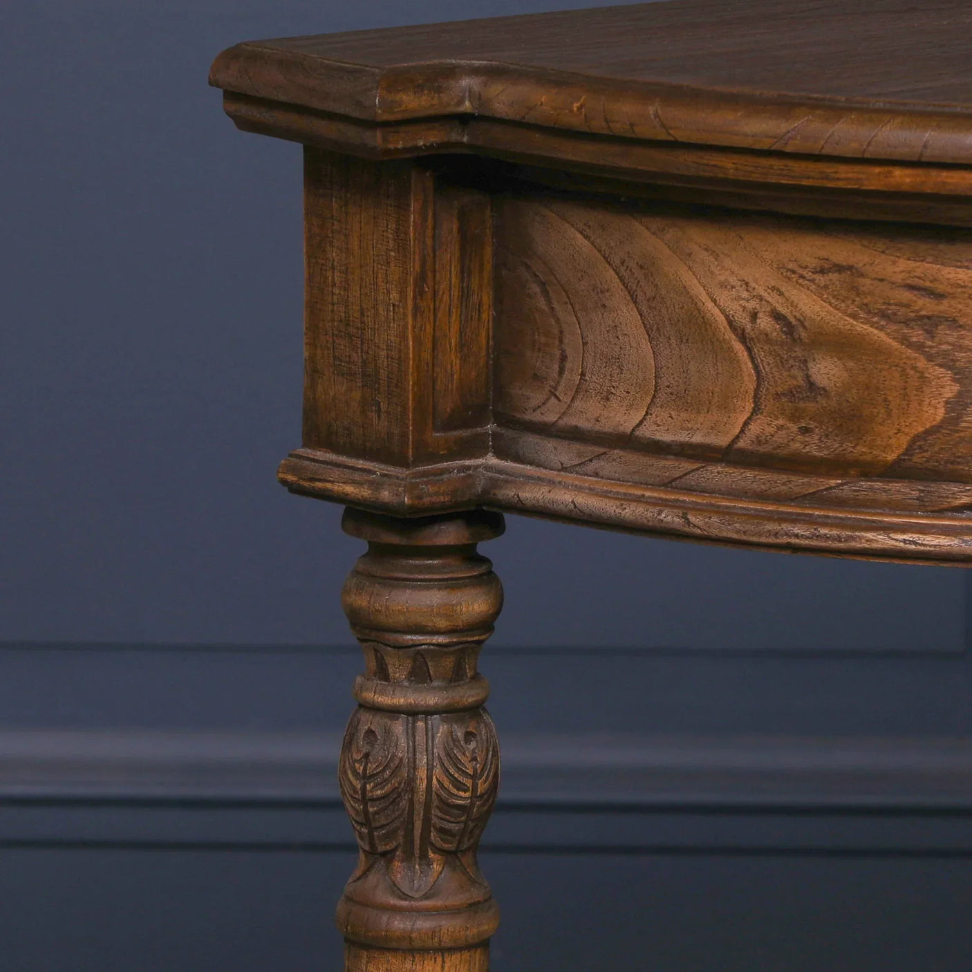 Carved wooden table leg and corner in dark oak finish against navy wall