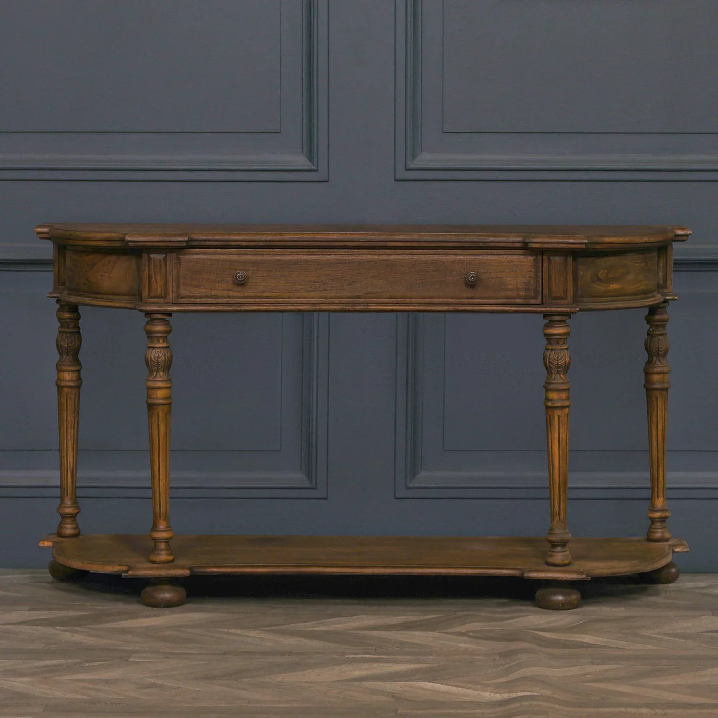 Antique wood console table with two drawers and carved legs against dark panel wall