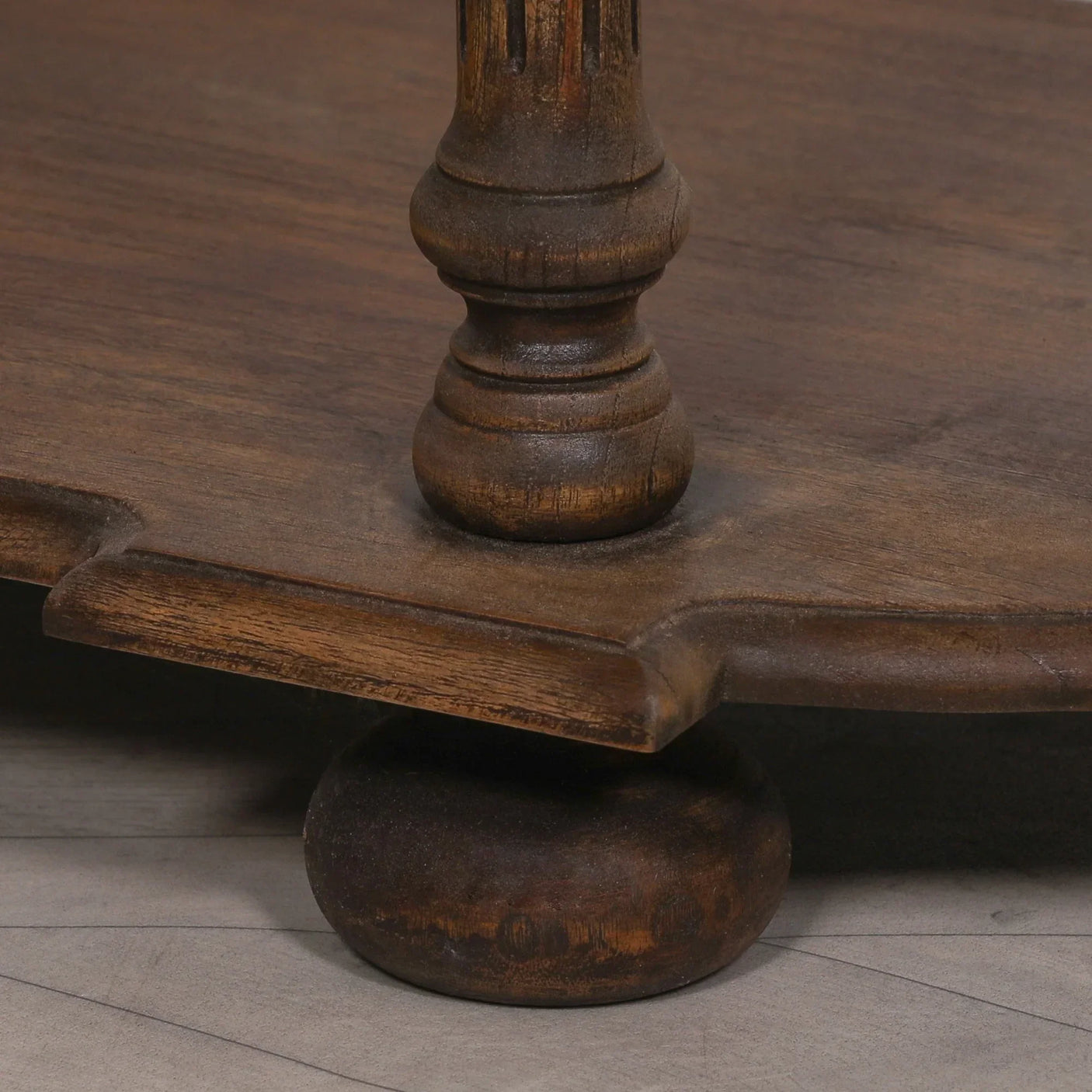 Close view of dark wood coffee table leg and scalloped edge on grey floor