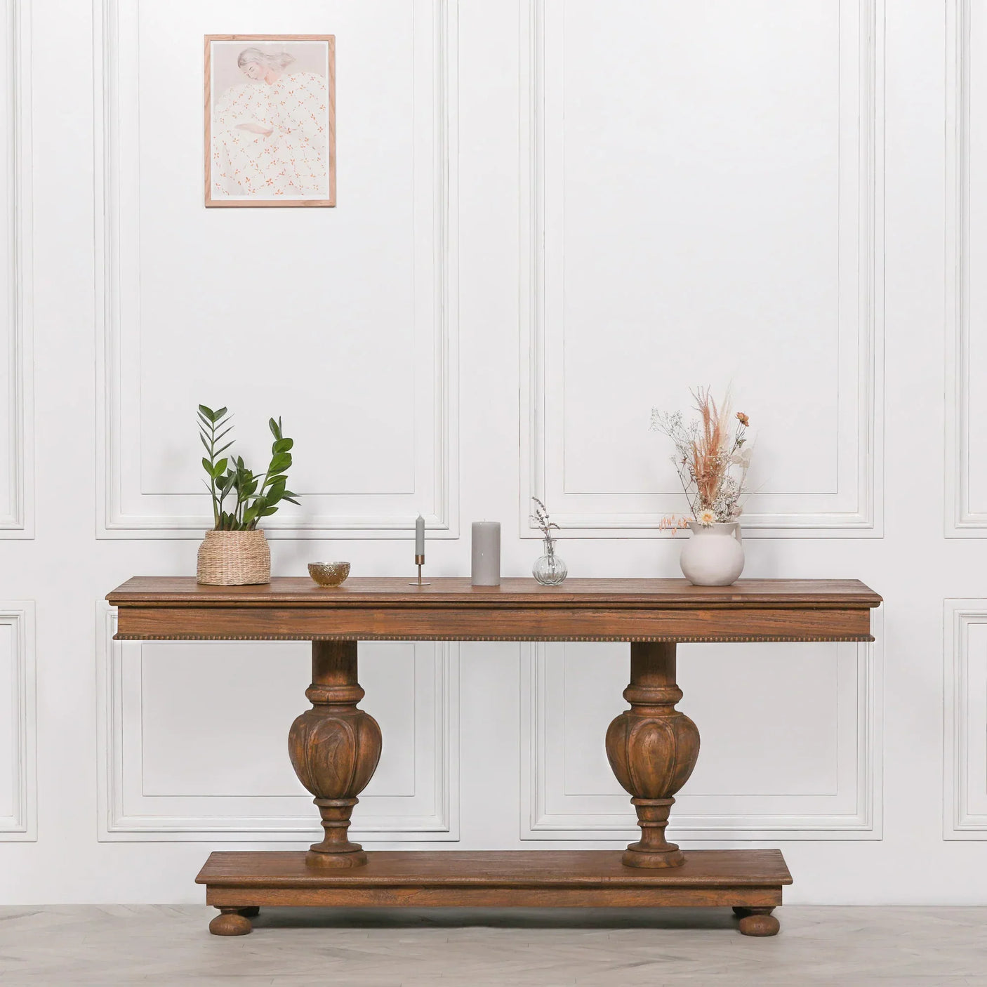 Solid wood console table with decorative vases and plants against white panel wall
