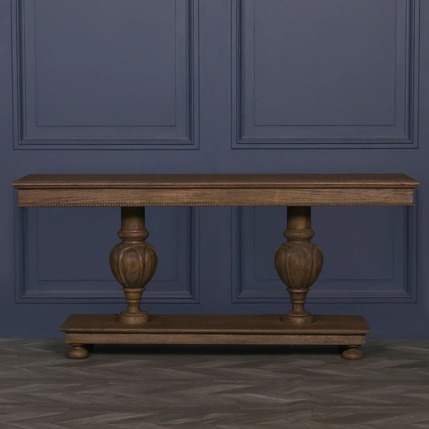 Wooden console table with ornate carved legs and a lower shelf against blue wall paneling
