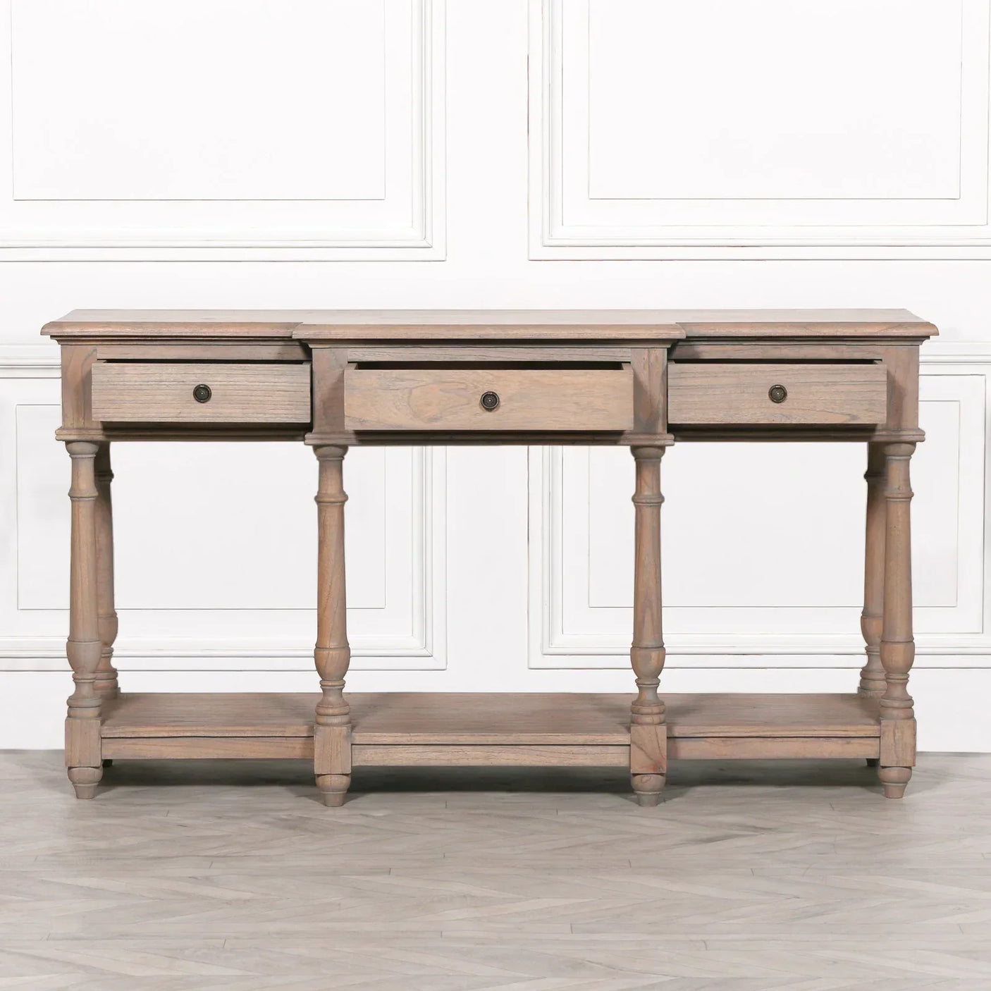 Wood console table with three drawers, turned legs and lower shelf against white wall