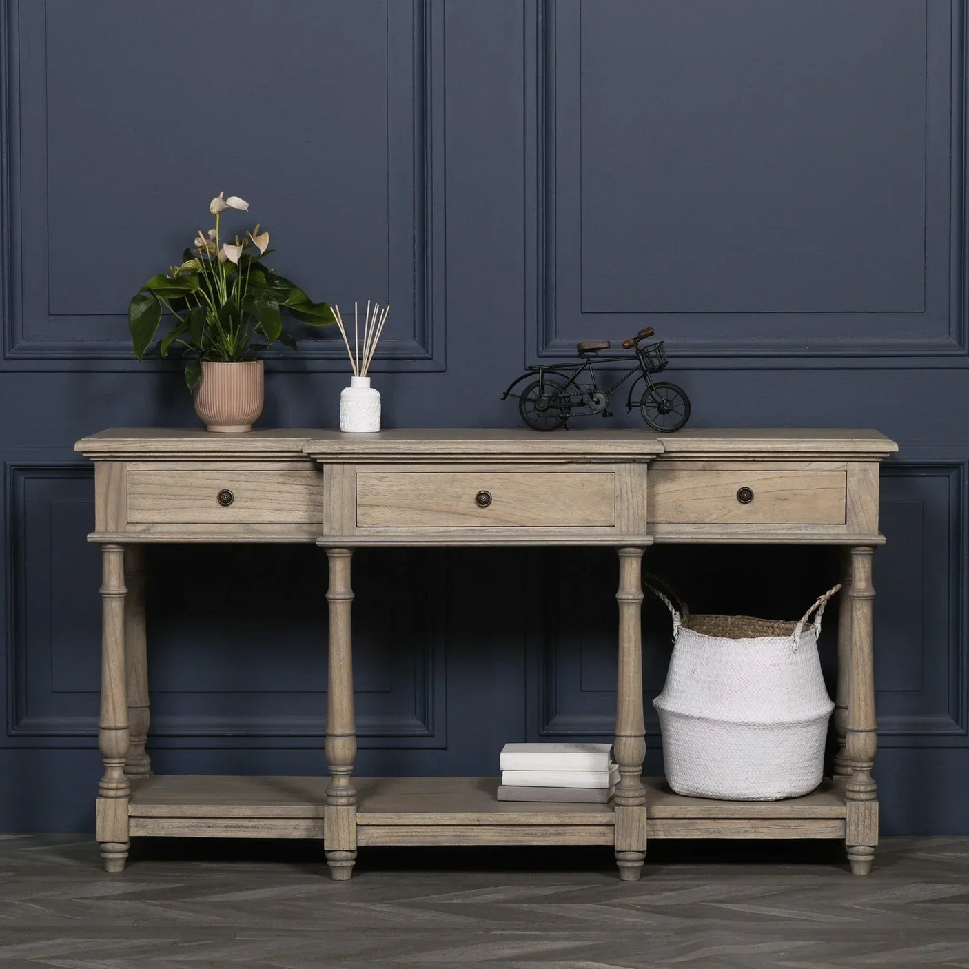 Wooden console table with three drawers, lower shelf, and decorative items against blue wall