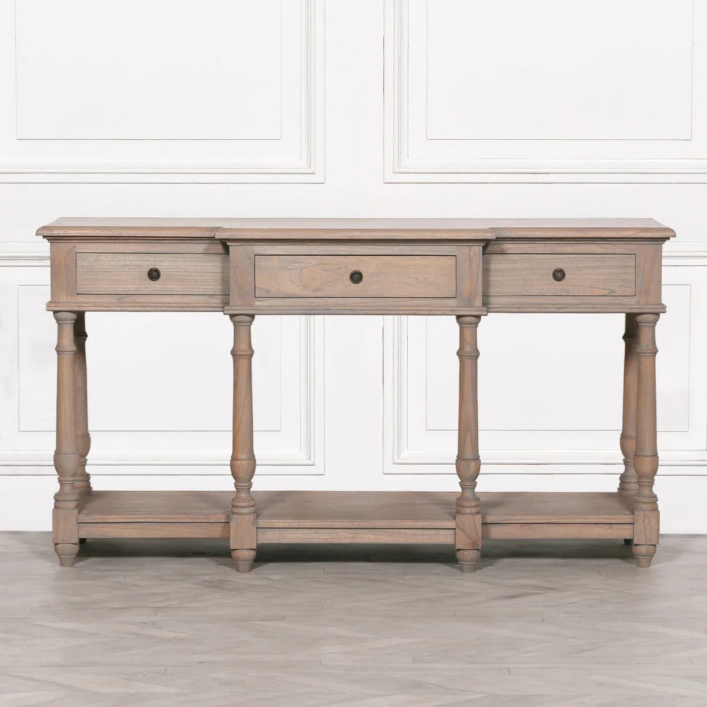 Wood console table with three drawers, turned legs, and lower shelf against white panel wall