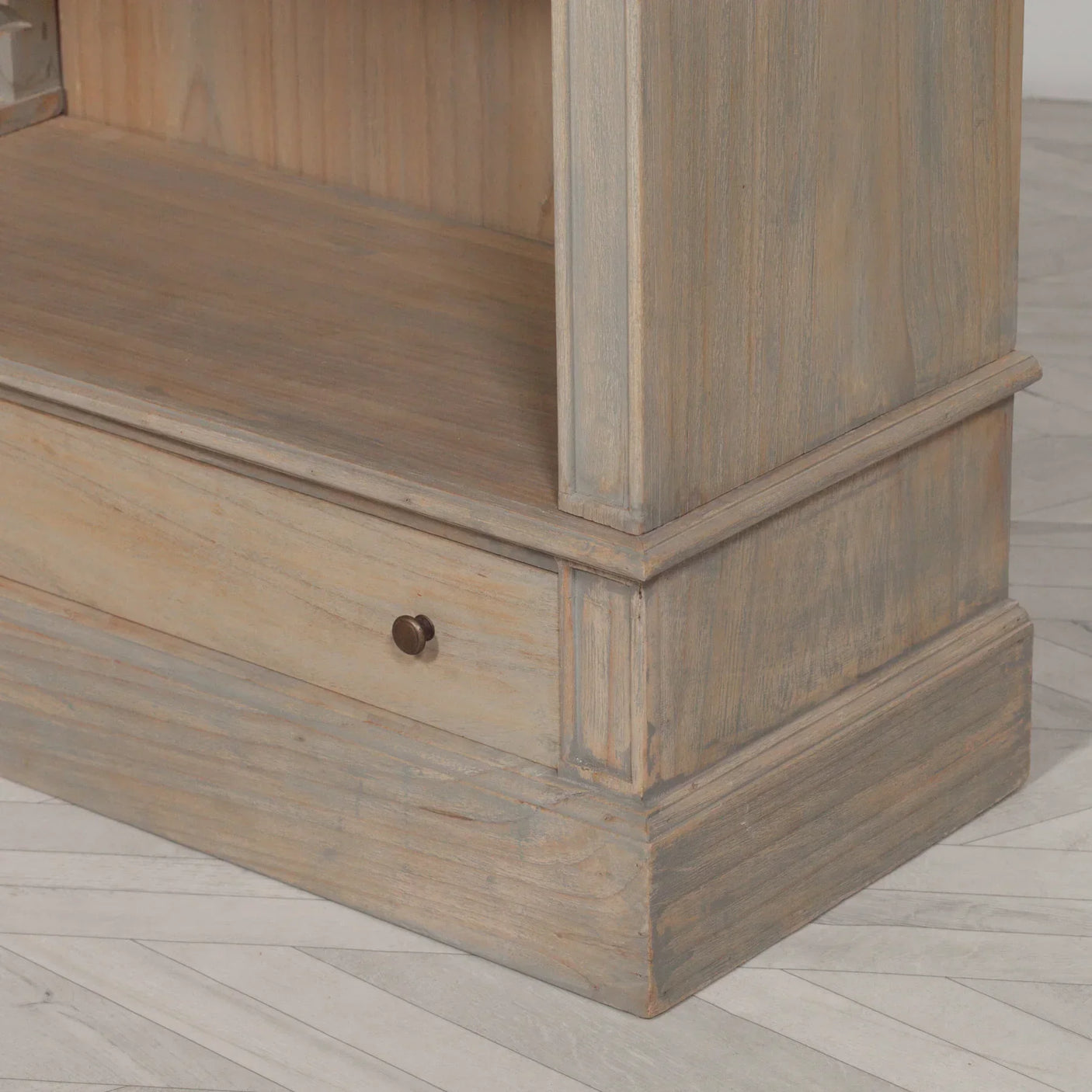 Light wood bookcase corner with lower storage drawer and visible brass handle