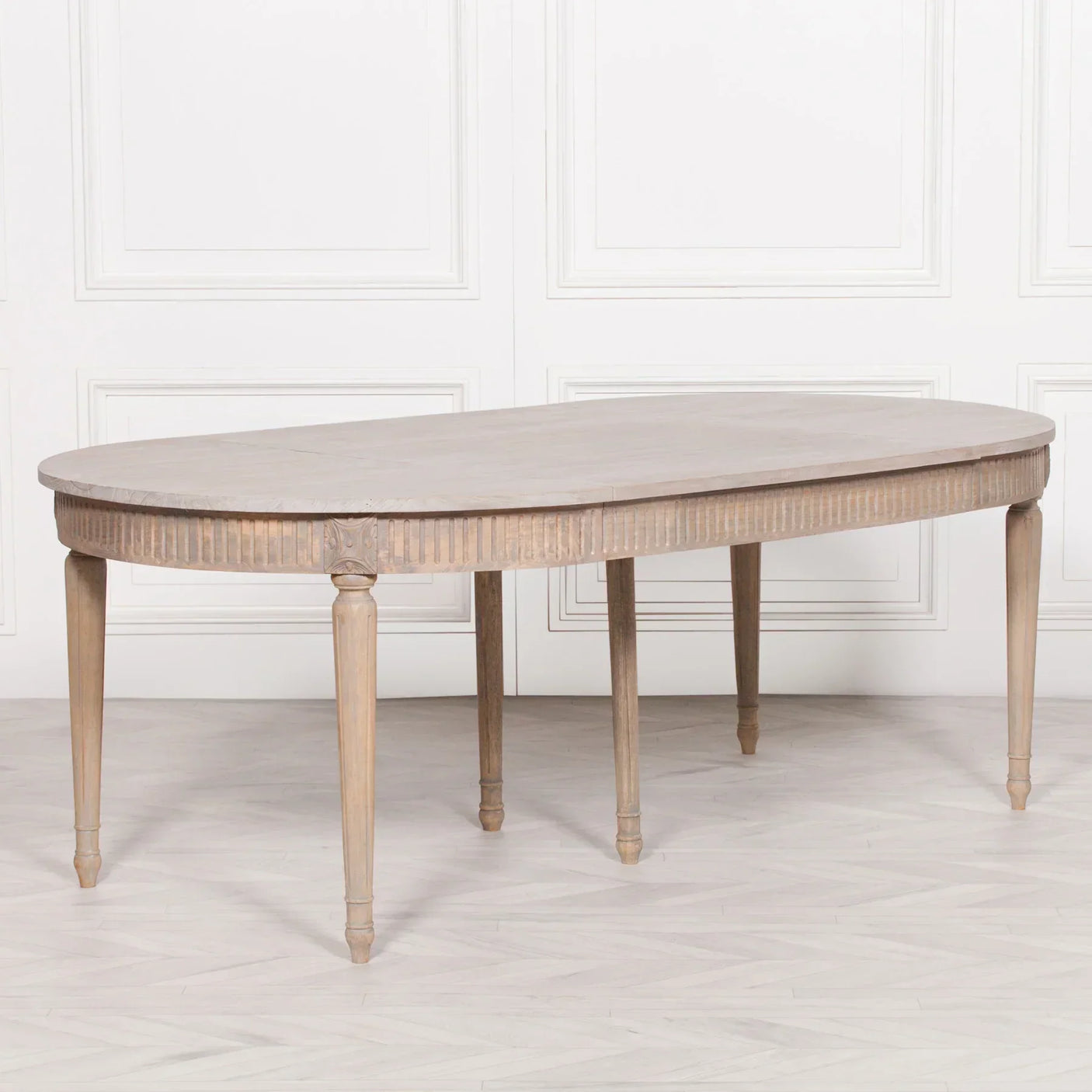 Oval wood dining table with carved apron and tapered legs in light finish