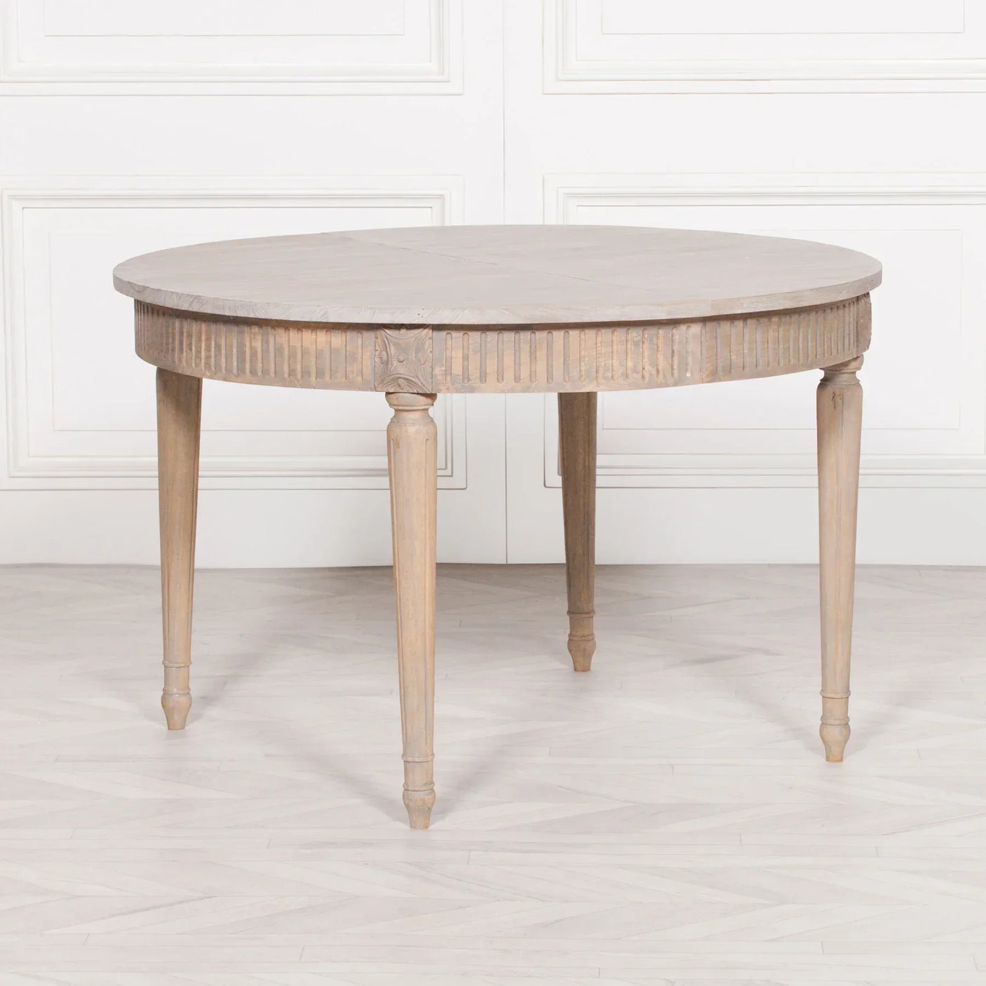 Round wooden dining table with carved legs and fluted apron on light floor