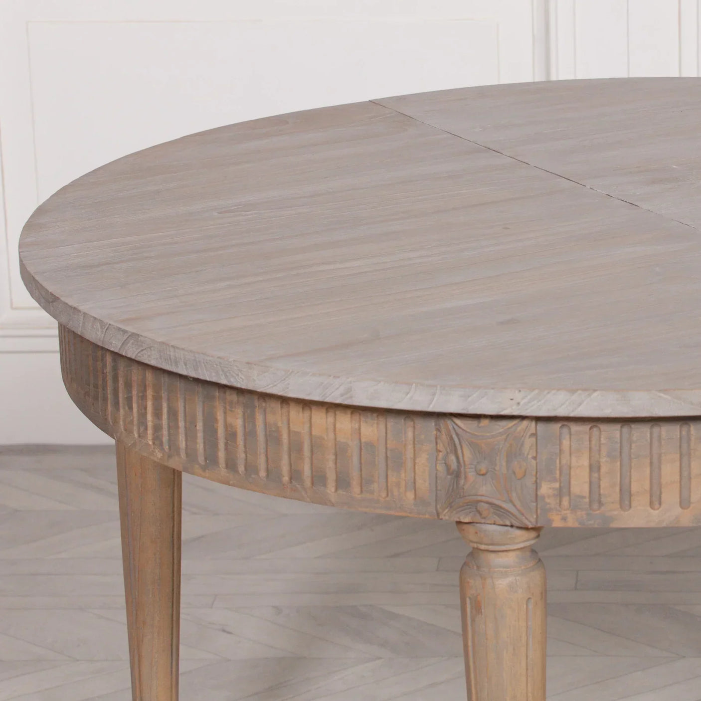 Round extendable wooden dining table with carved legs and fluted apron, close-up view
