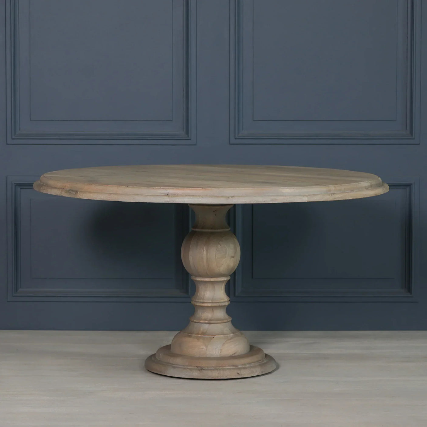 Round wooden dining table with carved pedestal base against a dark paneled wall