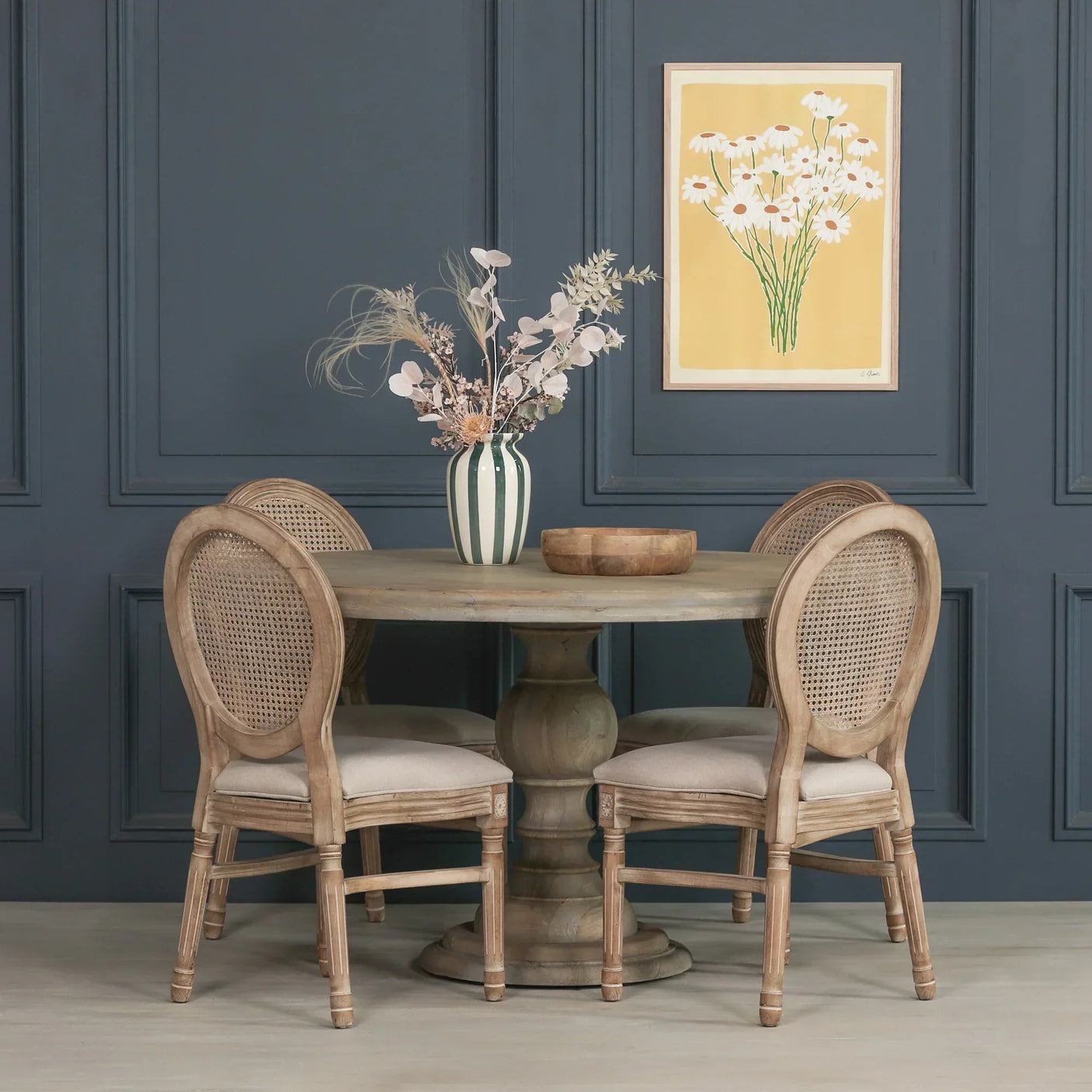 Round wooden dining table with four rattan back chairs and floral centerpiece
