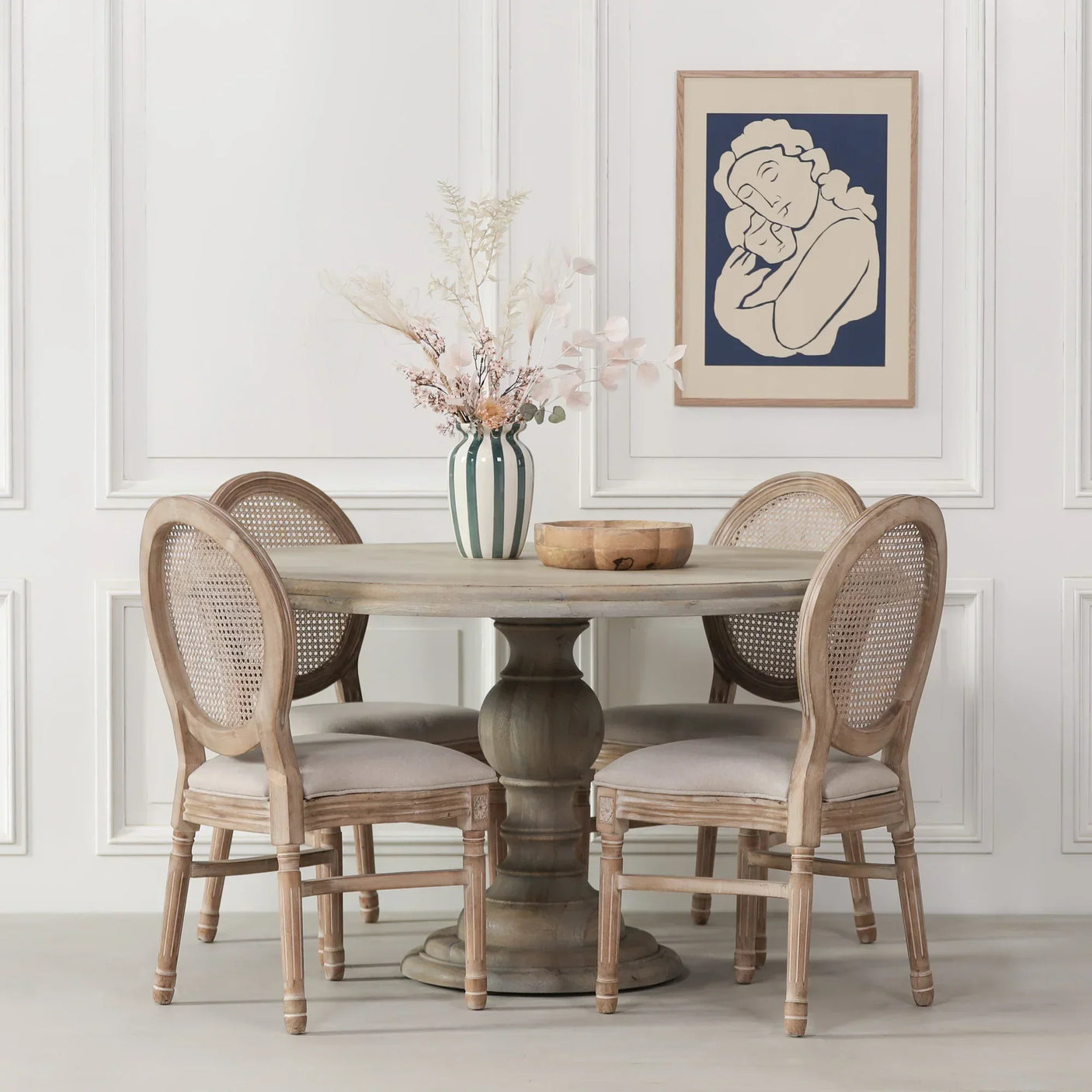Round wood dining table with four rattan-back chairs and vase centerpiece in modern room