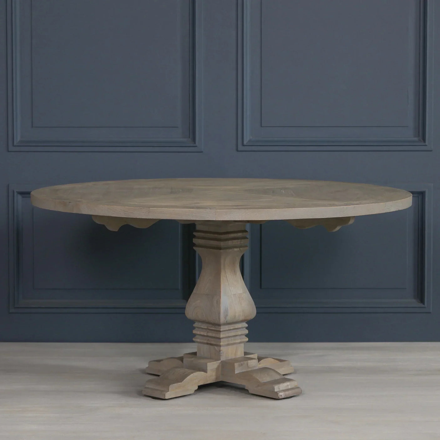 Round wooden dining table with pedestal base against dark paneled wall