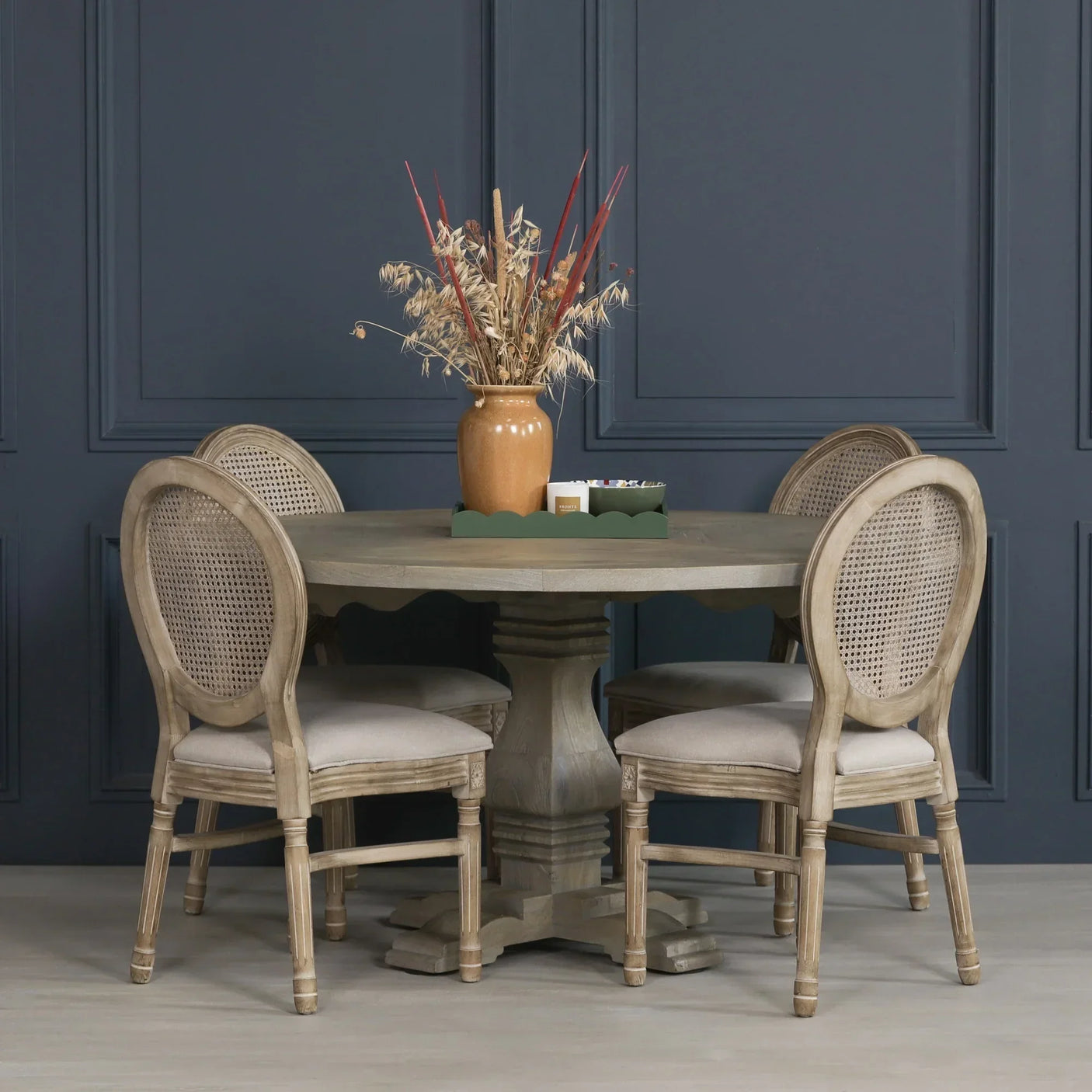 Round oak dining table with four rattan back chairs and neutral vase centerpiece