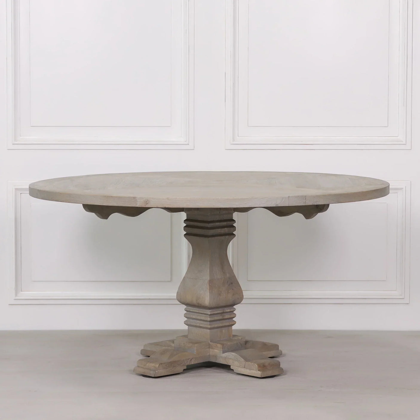 Round wooden dining table with pedestal base in a light finish against white wall