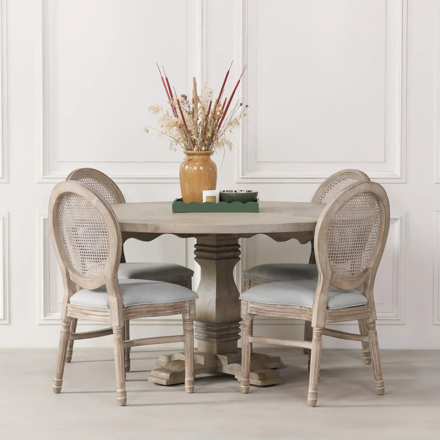 Round wooden dining table with four rattan back chairs and vase centerpiece
