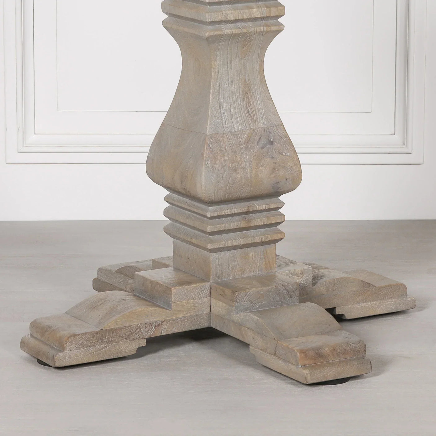 Solid wood dining table pedestal base with carved details on light flooring