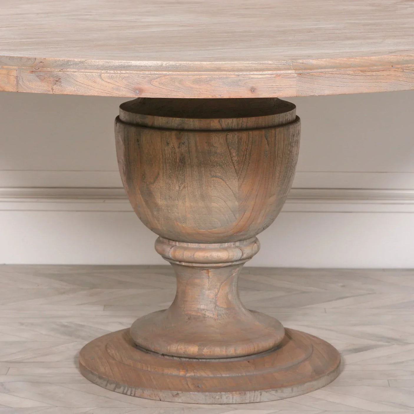 Round wooden dining table with pedestal base on herringbone floor