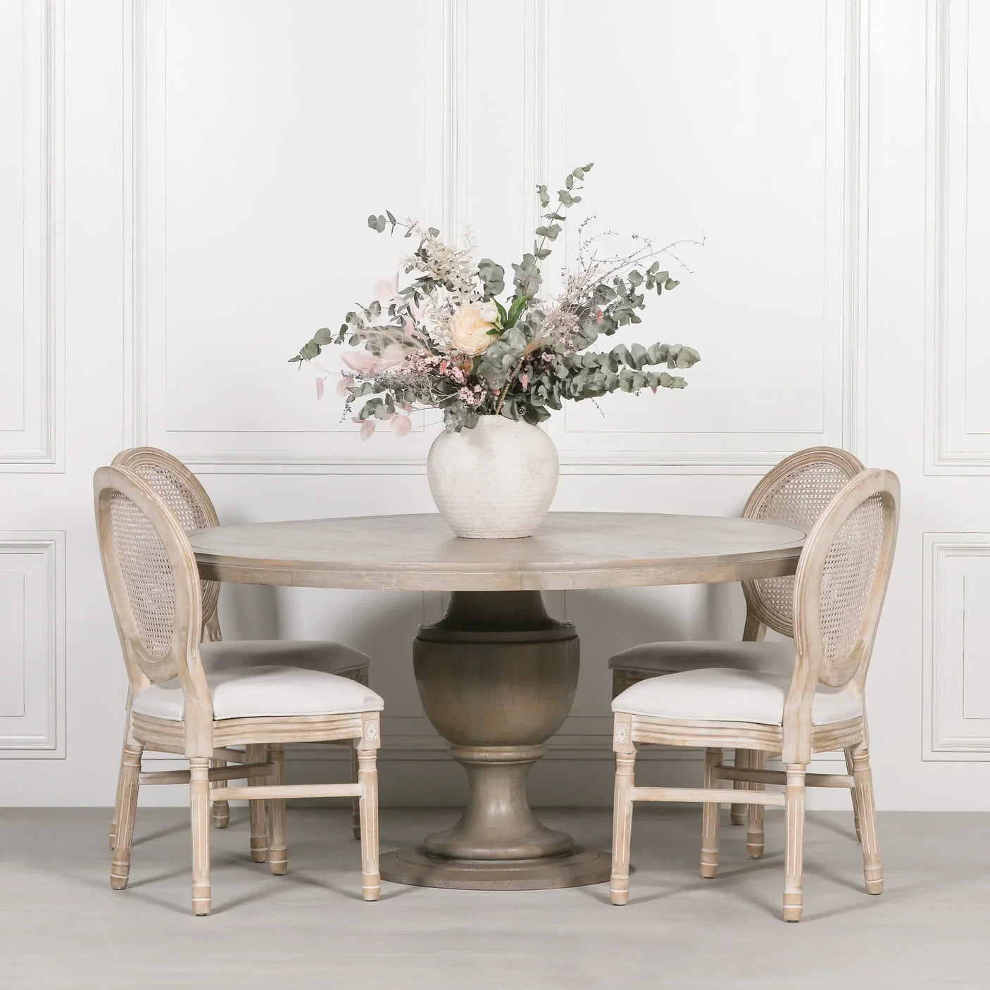 Round pedestal dining table with four cane-back chairs and floral centerpiece