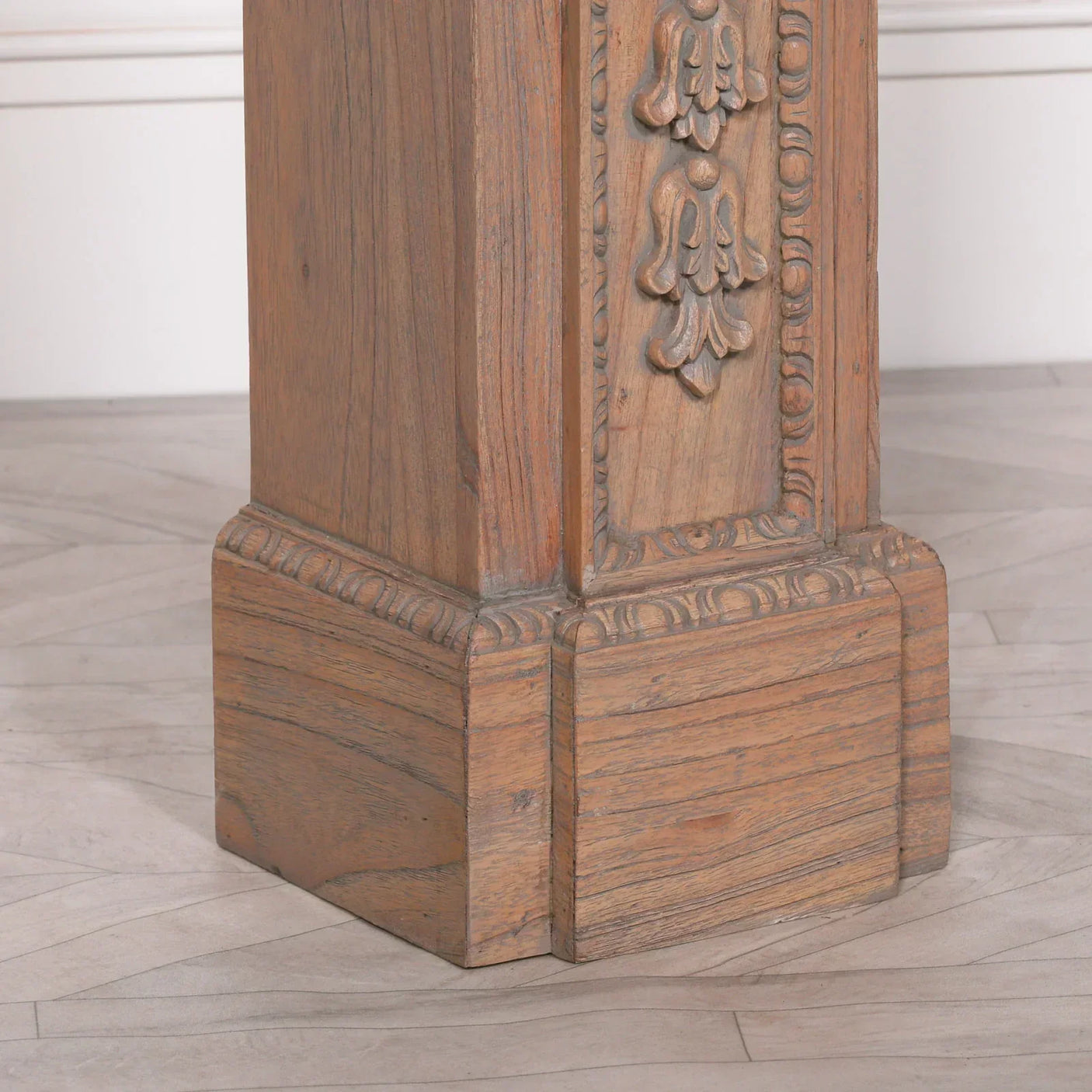 Carved wood table leg with ornate detailing and natural grain on light herringbone floor