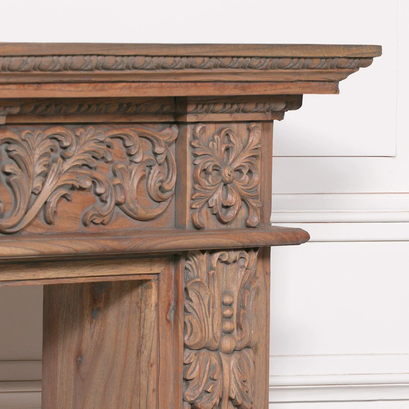 Carved wood fireplace surround with ornate floral and leaf detailing, close-up view