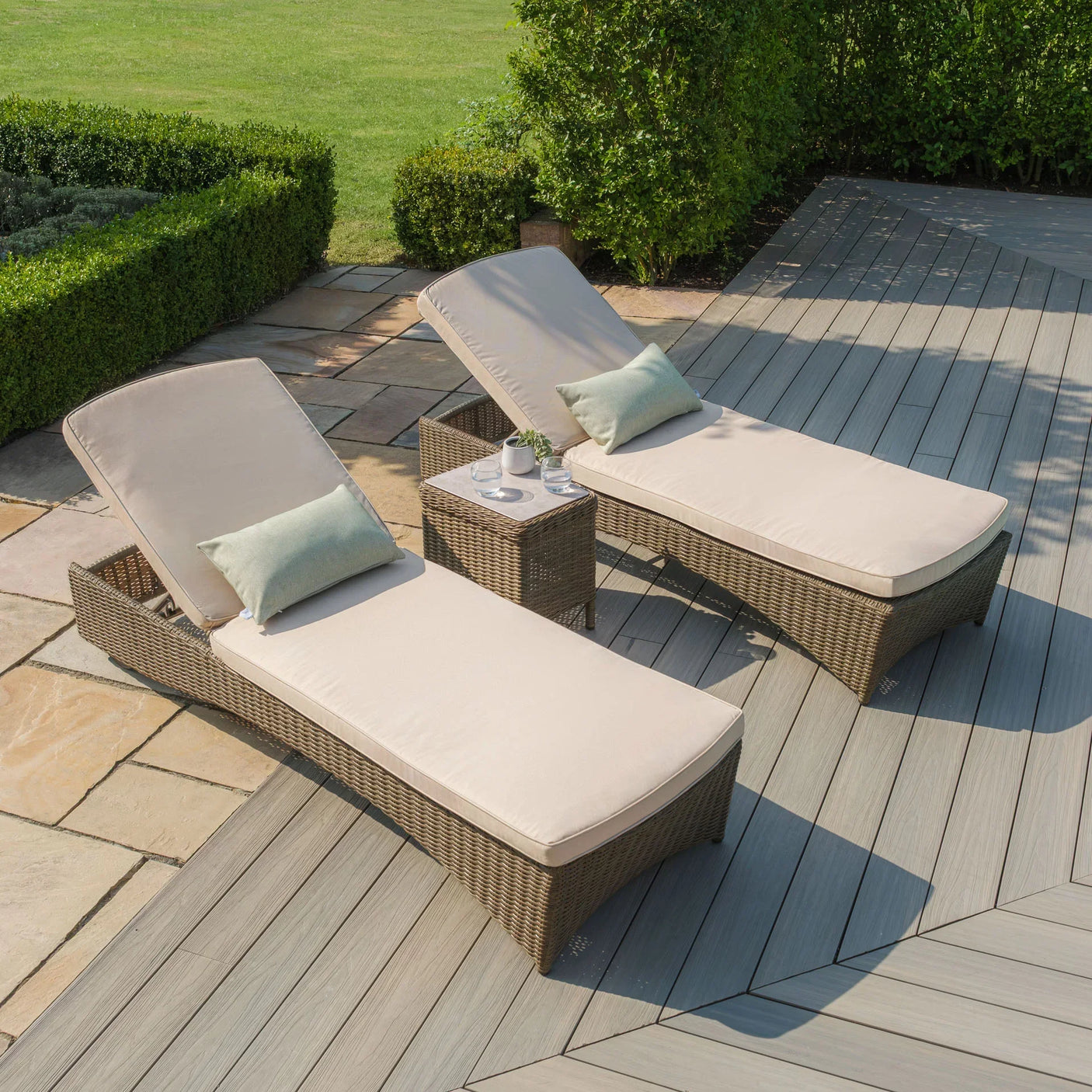 Rattan sun loungers with beige cushions and side table on a decked patio